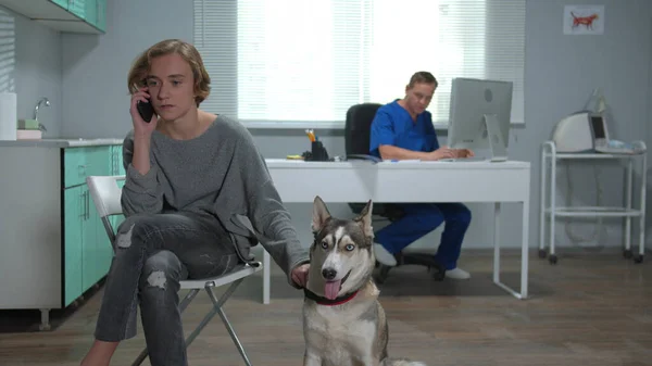 Man sits with husky and talks on phone in cabinet of vet — Stock Photo, Image