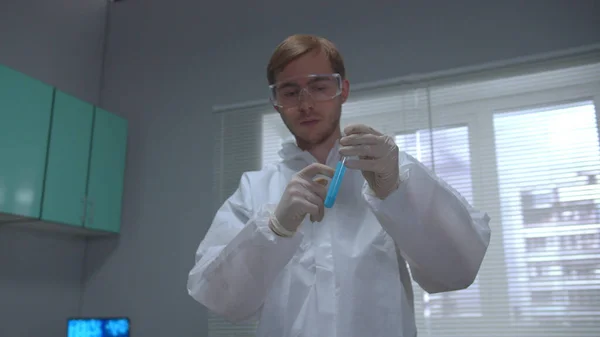 Científico en el tubo protector de la sacudida de la ropa de trabajo con el producto químico y lo aprieta en el laboratorio —  Fotos de Stock