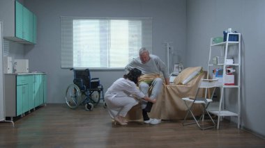Doctor in white uniform help old patient to get up from bed