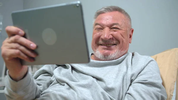 Adam hastanede yatağa uzanıp tabletten biriyle konuşuyor. 