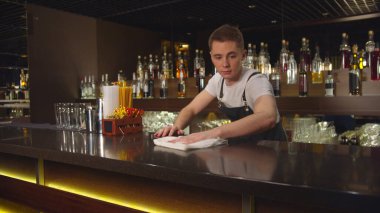 Bartender in the apron wipes bar counter with a rag