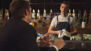 Man sits at the bar, holds credit card and talks to bartender 