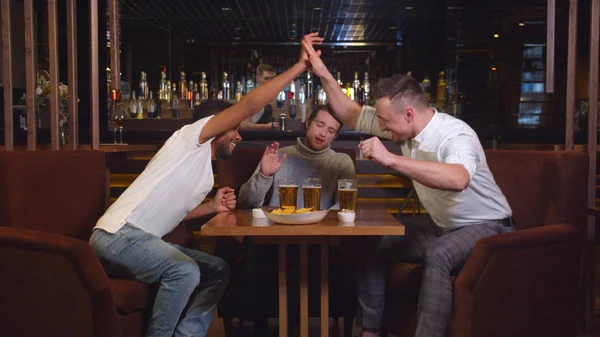 Barátok ülnek a bárban, söröznek és focit néznek a fogadáson. — Stock Fotó