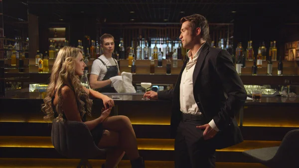 Man in suit talks with woman and gives her a cocktail at the bar