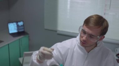 Slow motion, chemist in protective workwear shake tube with blue liquid in the laboratory
