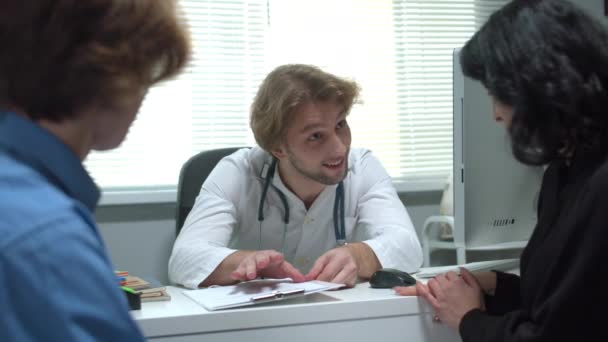 Médico hablar amistoso con el niño y la madre en el gabinete del hospital, cámara lenta — Vídeo de stock