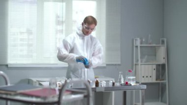 Yavaş çekim, koruyucu giyimli ve tıbbi eldivenli adam laboratuarda tüpü aç.