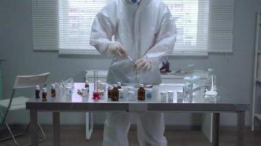 Koruyucu iş elbisesi giyen bir adam laboratuarda çubukla tüpe dokunuyor.