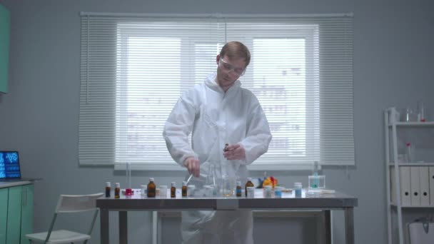 Вид спереди, человек в защитной рабочей одежде берет химикат из пробирки в лаборатории — стоковое видео