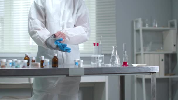 Hombre en ropa de trabajo protectora ponerse guantes médicos en el laboratorio — Vídeos de Stock