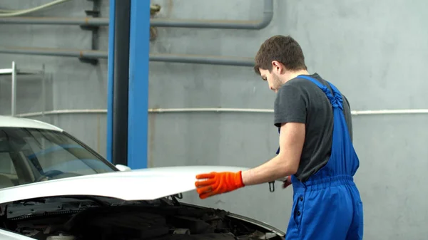 Mechanic closes hood of car and looks at the camera — Stockfoto