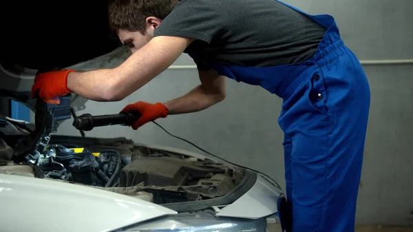 Mechanic with flashlight examines the motor of car — Stock Photo, Image