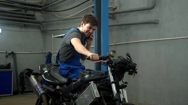 Slow motion, technician sits on motorcycle and talks on phone