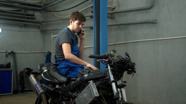Technician sits on motorcycle and talks on phone