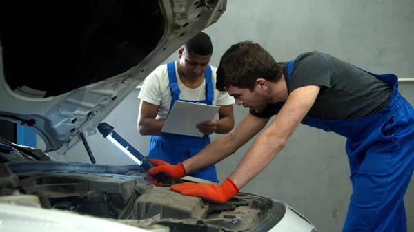 Mechanic examines the motor of car and his collegue takes notes — Stock Photo, Image