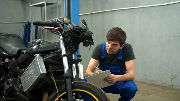 Techniker repariert Motorrad und macht sich Notizen — Stockfoto