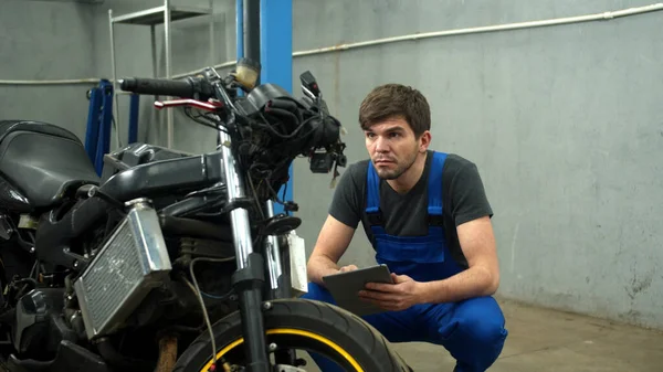 Mekanik dengan tablet mencoba untuk memperbaiki sepeda motor di layanan mobil — Stok Foto