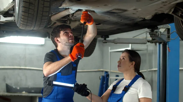 Mekaniker i handskar reparerar en bil, kvinna håller en ficklampa — Stockfoto