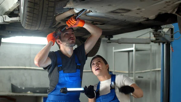 Slow motion, mechanic in gloves repairs a car, woman holds a flashlight