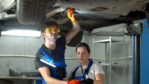 Mechanic in glasses repairs a car, woman holds a flashlight