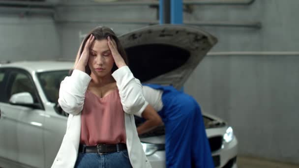 Mechanic repairs a car, indignant woman looks at the camera — 图库视频影像