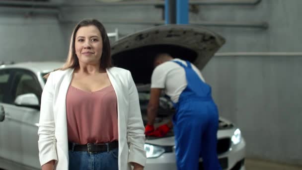 Mechanic repairs a car, woman smiles at the camera — 图库视频影像