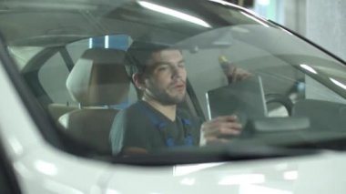 Mechanic with a tablet sits in a car and checks it