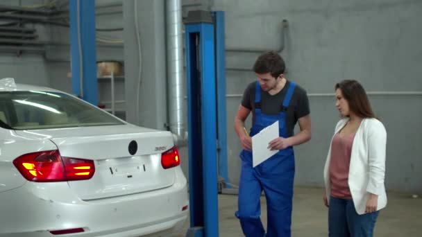 Mecánico muestra daños en el coche a una mujer — Vídeo de stock