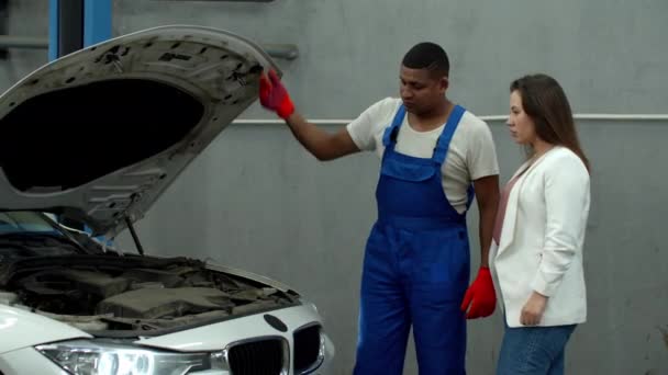 Mechanik otwiera maskę samochodu i pokazuje silnik kobiecie — Wideo stockowe