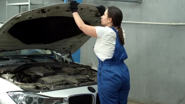 Woman mechanic closes hood of car and smiles in car service — Stockvideo