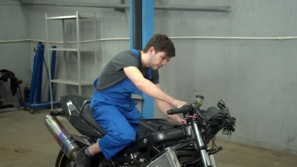 Slow motion, tekniker sitter på motorcykel och reparerar den — Stockvideo