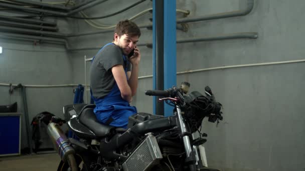 Αργή κίνηση, τεχνικός κάθεται στη μοτοσικλέτα και μιλάει στο τηλέφωνο — Αρχείο Βίντεο