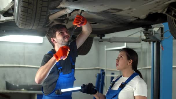 Mechanic in gloves repairs a car, woman holds a flashlight — Stock Video