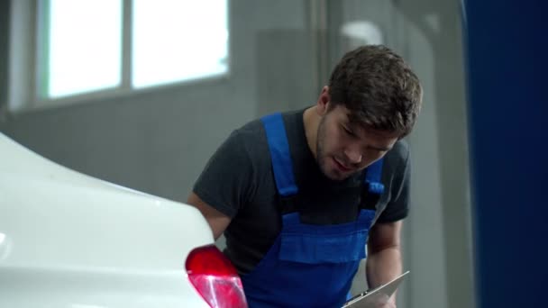 Mecánico inspecciona los faros de un coche y escribe algo — Vídeos de Stock