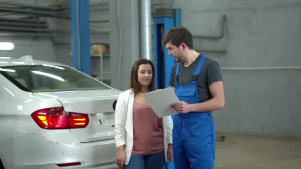 Mujer discute el precio de una reparación de coche con un mecánico — Vídeos de Stock