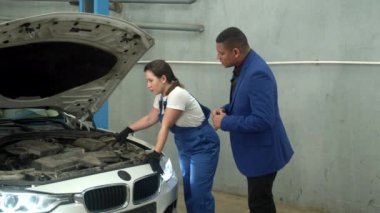 Kadın teknisyen araba tamircisine bir araba gösteriyor.