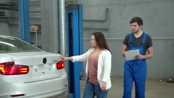 Woman shows to mechanic the zones of a bang on a car — ストック動画