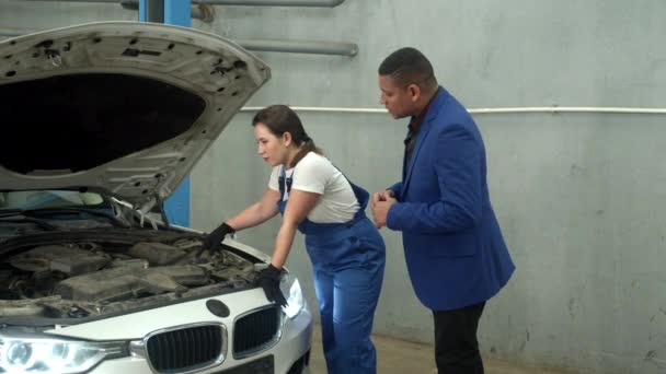 Mujer técnico muestra un coche al propietario en taller de reparación de automóviles — Vídeos de Stock