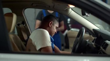 Mechanic with a tablet gets into a car and tells to colleague to take notes