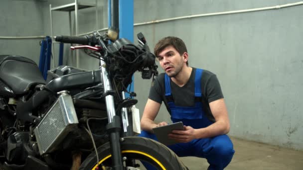Mekaniker med surfplatta försöker reparera en motorcykel i bilservice — Stockvideo