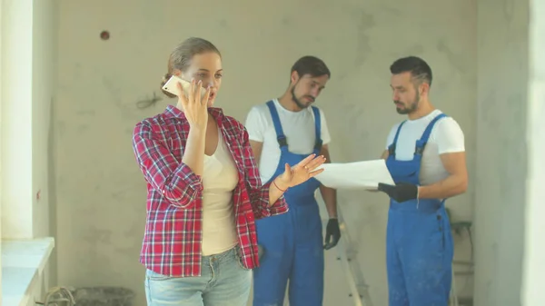 Woman records a voice message, repairmen stands on the background