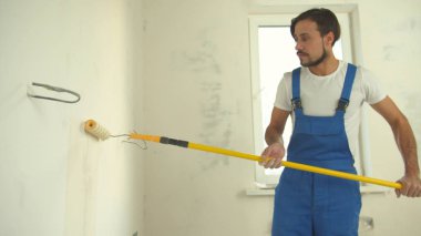 Üniformalı tamirci daireye duvar boyuyor.