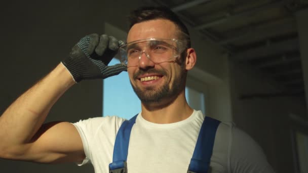 Constructor sonriente se para y se quita las gafas protectoras, cámara lenta — Vídeos de Stock