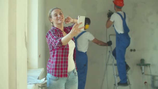 Mujer feliz hace una foto, los constructores trabajan en el fondo — Vídeos de Stock