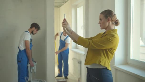 Mujer hace una foto en el teléfono, reparadores trabajan en el piso — Vídeo de stock