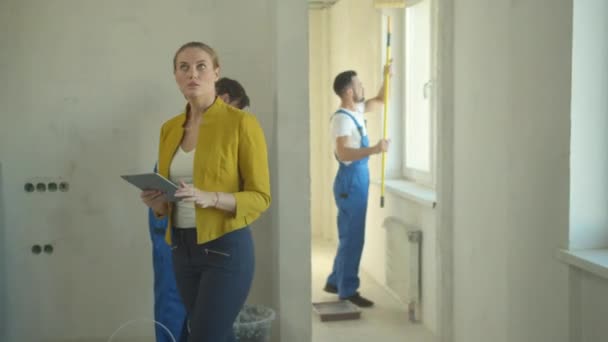 Mujer camina con la tableta, reparadores trabajan en el piso — Vídeo de stock