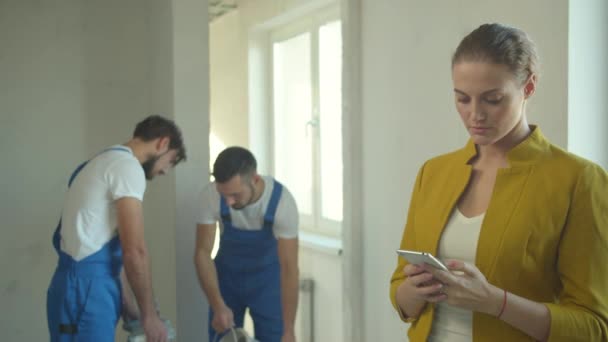Vrouw neemt een foto op de telefoon, bouwers werken in de flat — Stockvideo