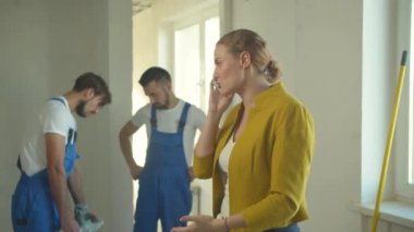 Kadın telefonda duygusal konuşur, inşaatçılar üniformalı çalışır.