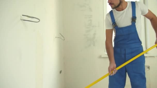 Reparador en uniforme pinta una pared en el piso — Vídeos de Stock