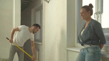 Erkek duvarı boyar, kadın onunla konuşur ve gülümser.